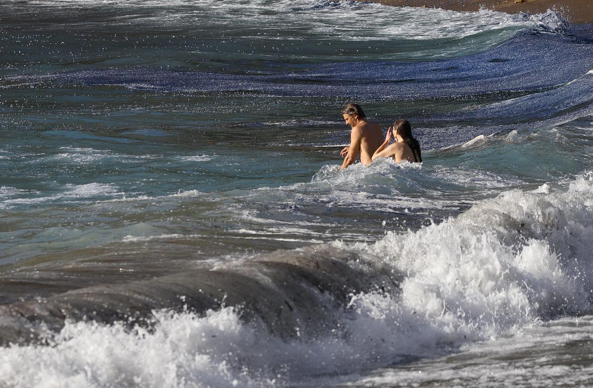 Dos bañistas en Benirràs junto a una marea azul de medusas velero.